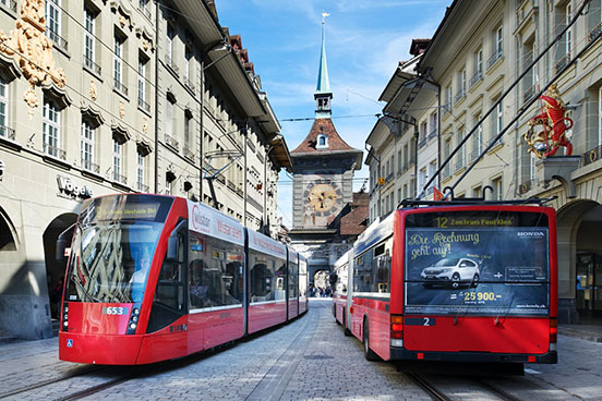 Ein rotes Tram kreuzt einen roten Bus in Berns Marktgasse