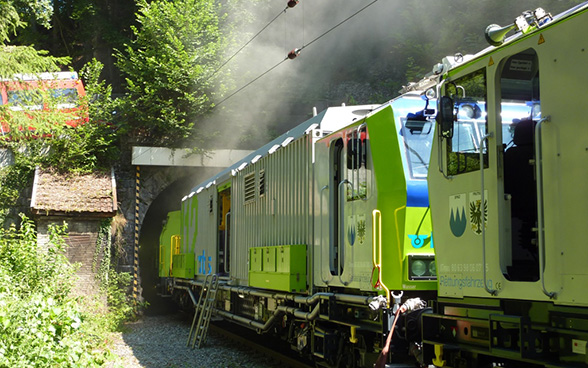 Le train d’extinction et de sauvetage vert du BLS stationne devant l’entrée d’un tunnel d’où sort de la fumée. 