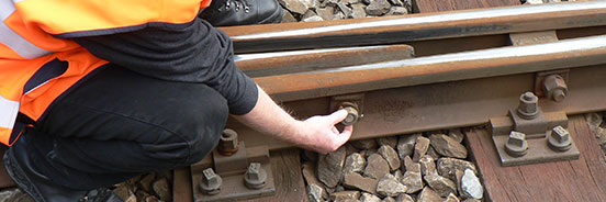 Ein Bahnarbeiter überprüft eine Schraubenmutter eines Gleises.