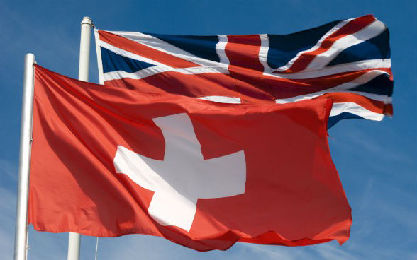 Eine Schweizer Flagge und eine der UK wehen im Wind.
