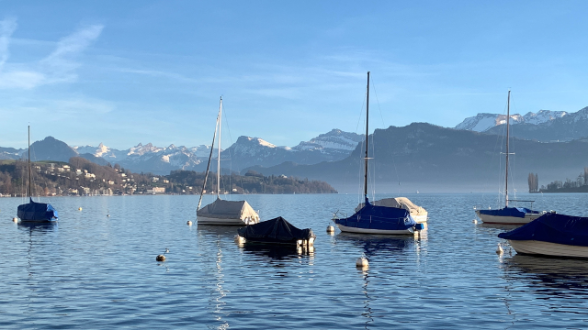 Abgedeckte Boote liegen an drei Molen in einem See, der am Fuss eines Hügels liegt.