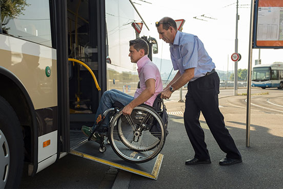 Einem Rollstuhlfahrer wird an einer Haltestelle in den Bus geholfen.