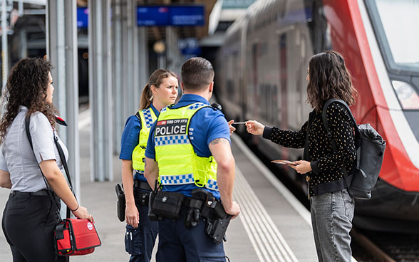 Une usagère en discussion avec deux collaborateurs en uniforme de la police des transports.