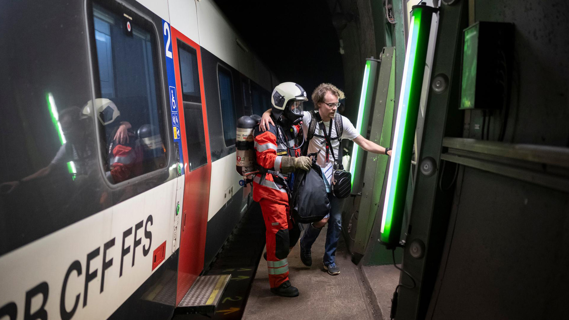 Moderna galleria ferroviaria a doppio binario, con accesso alla via di evacuazione illuminato di verde.